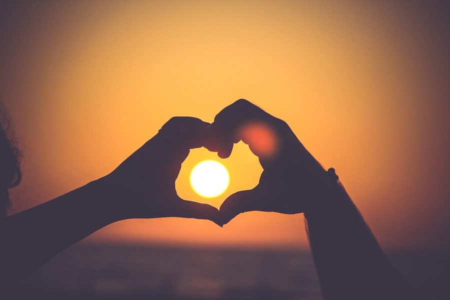 Two hands forming a heart against the setting sun